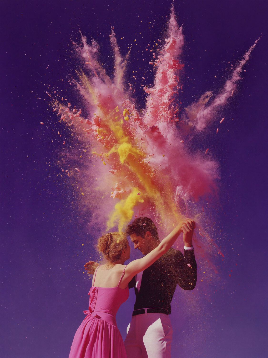 A couple dances in a cloud of yellow and pink powder against a violet sky.