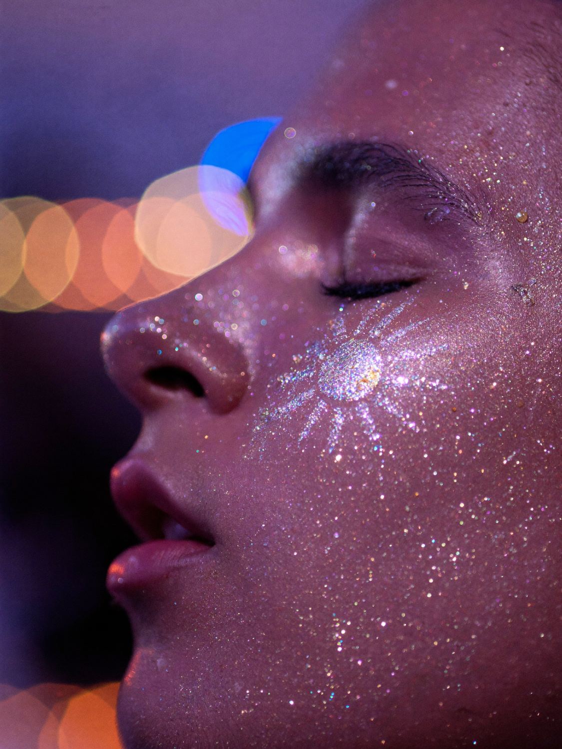 Close-up of a face with eyes closed and a sun drawn in glitter on the cheek.