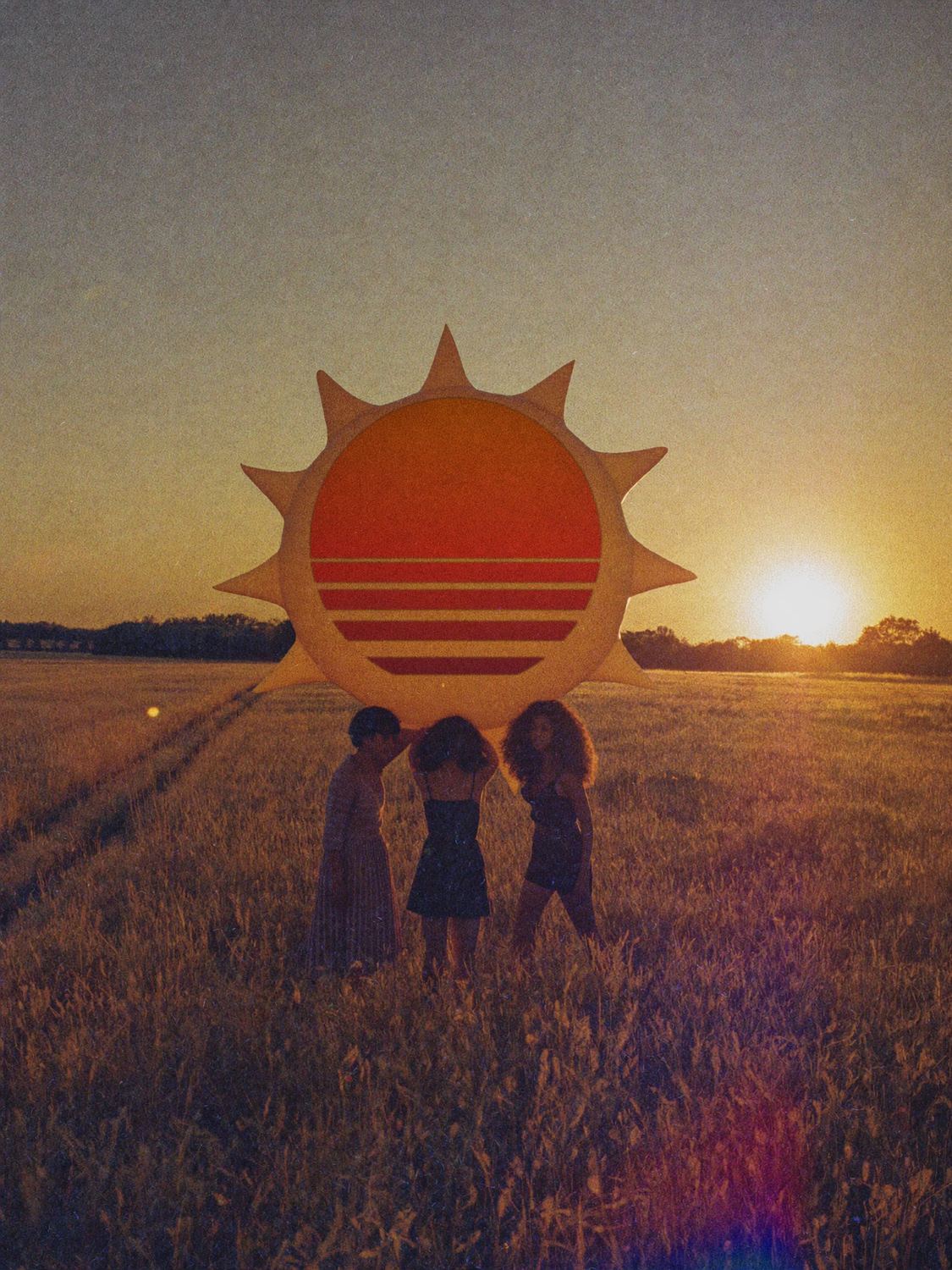 Three people carry a giant inflatable sun across a field at sunset. The SOLSTICE sun mark is printed on its face.