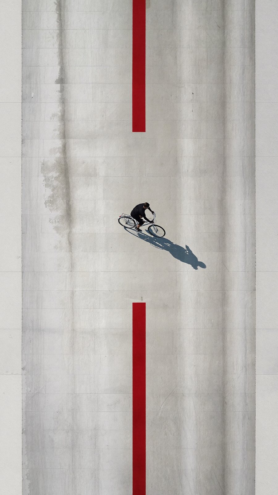 Top view of a cyclist riding along a red line on pale concrete