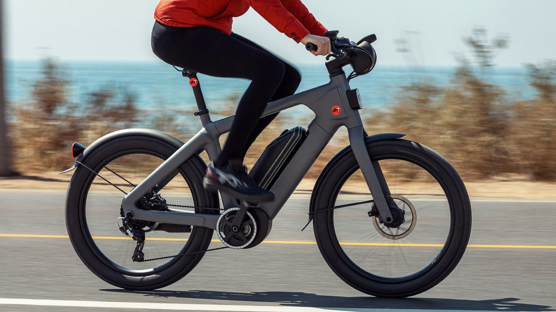 Cyclist in a red jacket riding a grey e-bike along a coast road