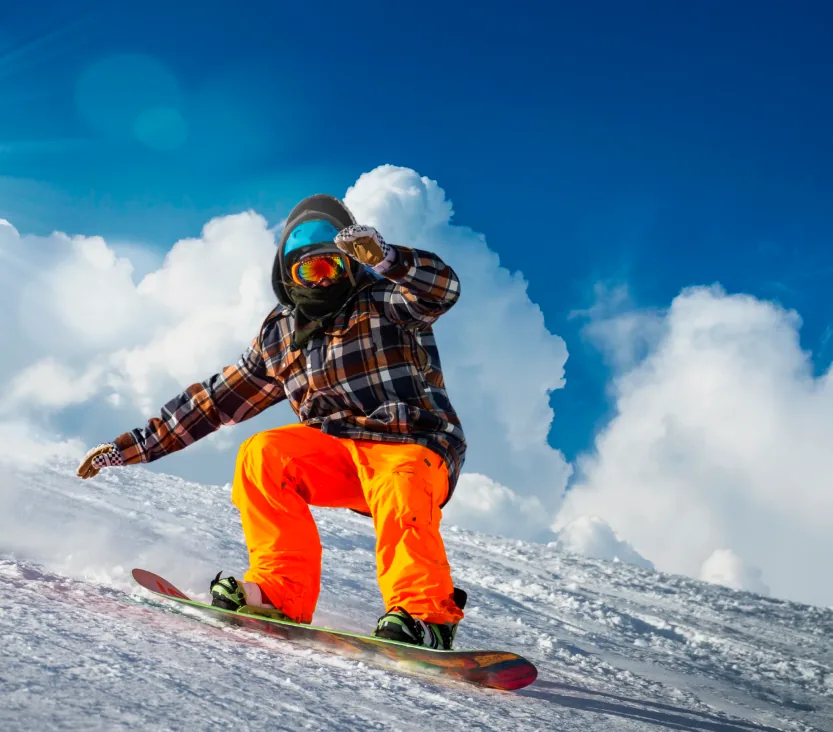 A snowboarder in an orange snowsuit carving a turn under blue sky