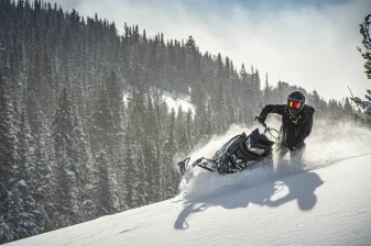 A snowmobile kicking up snow in a pine forest