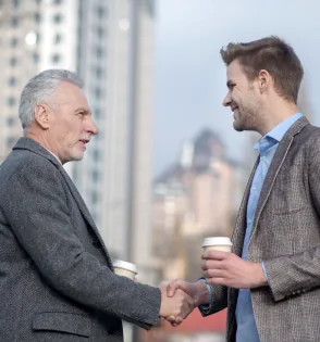 Two men shaking hands over coffee in a city