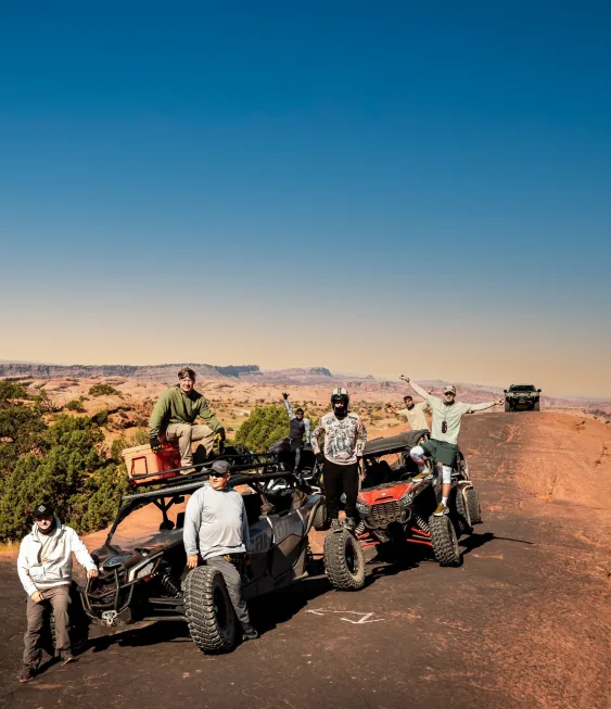 A group of men with off-road buggies on red desert rock under a blue sky