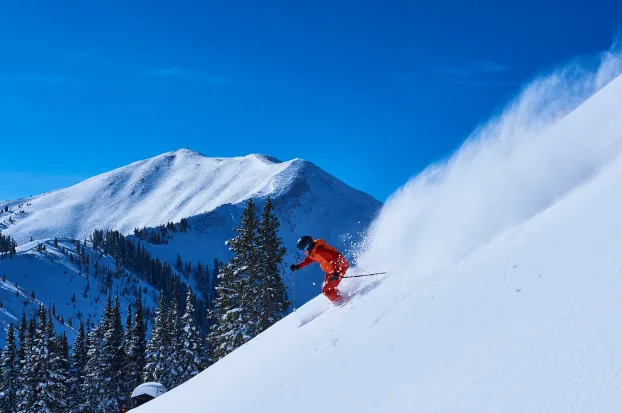 A skier carving through deep powder below a snowy peak