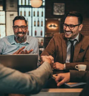 Two colleagues in a bar shaking hands over a laptop