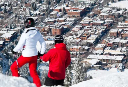 Two skiers in red looking over the town of Aspen from a ridge