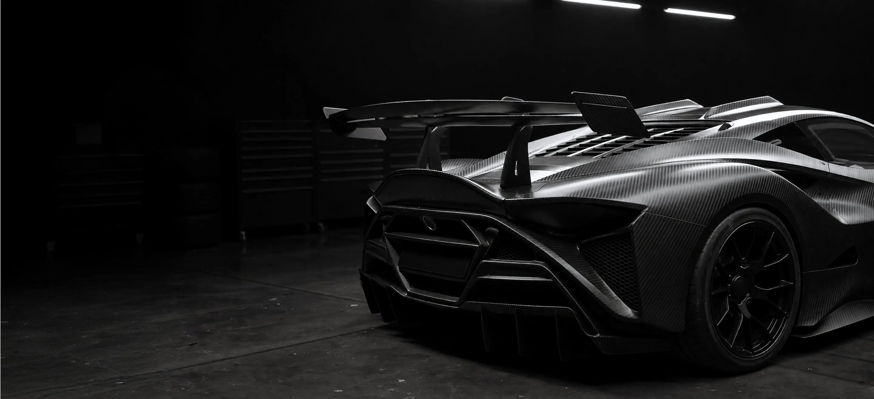 Carbon fiber race car seen from the rear in a dark garage