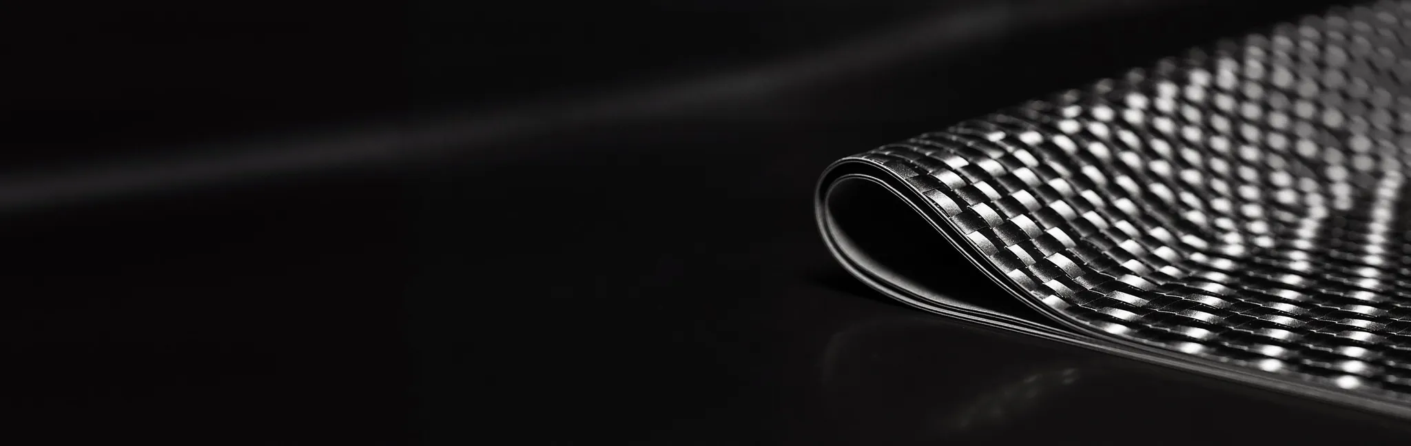 Sheet of carbon fiber composite with a visible weave on a dark background
